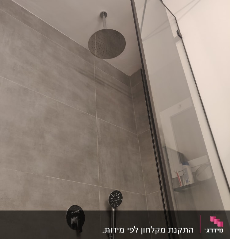 ראש מקלחת עגול עם ידית מקלחת על קיר אפור